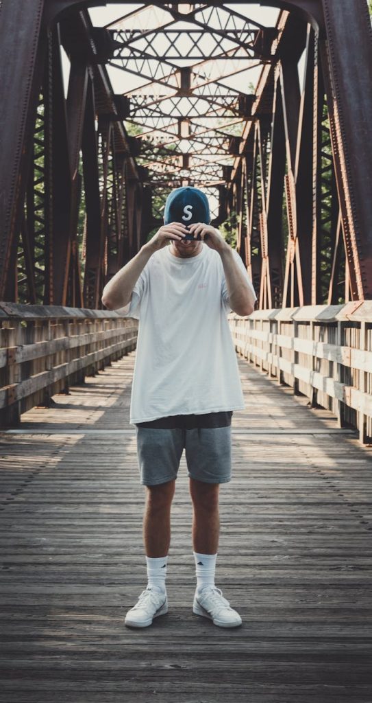 Casual fashion photo of a man posing on a metal bridge on a sunny day.