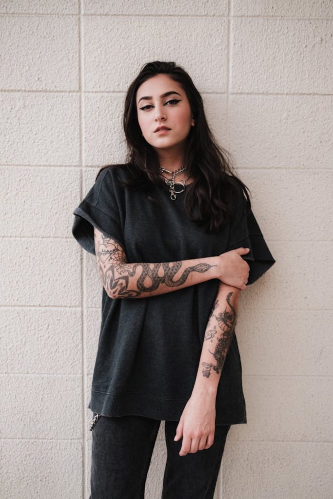 Casually styled model in streetwear posing against a textured wall displaying edgy tattoos.